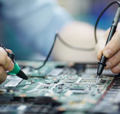 Closeup shot of male hands testing electric current voltage in circuit board of disassembled laptop using multimeter tool on table in maintenance shop